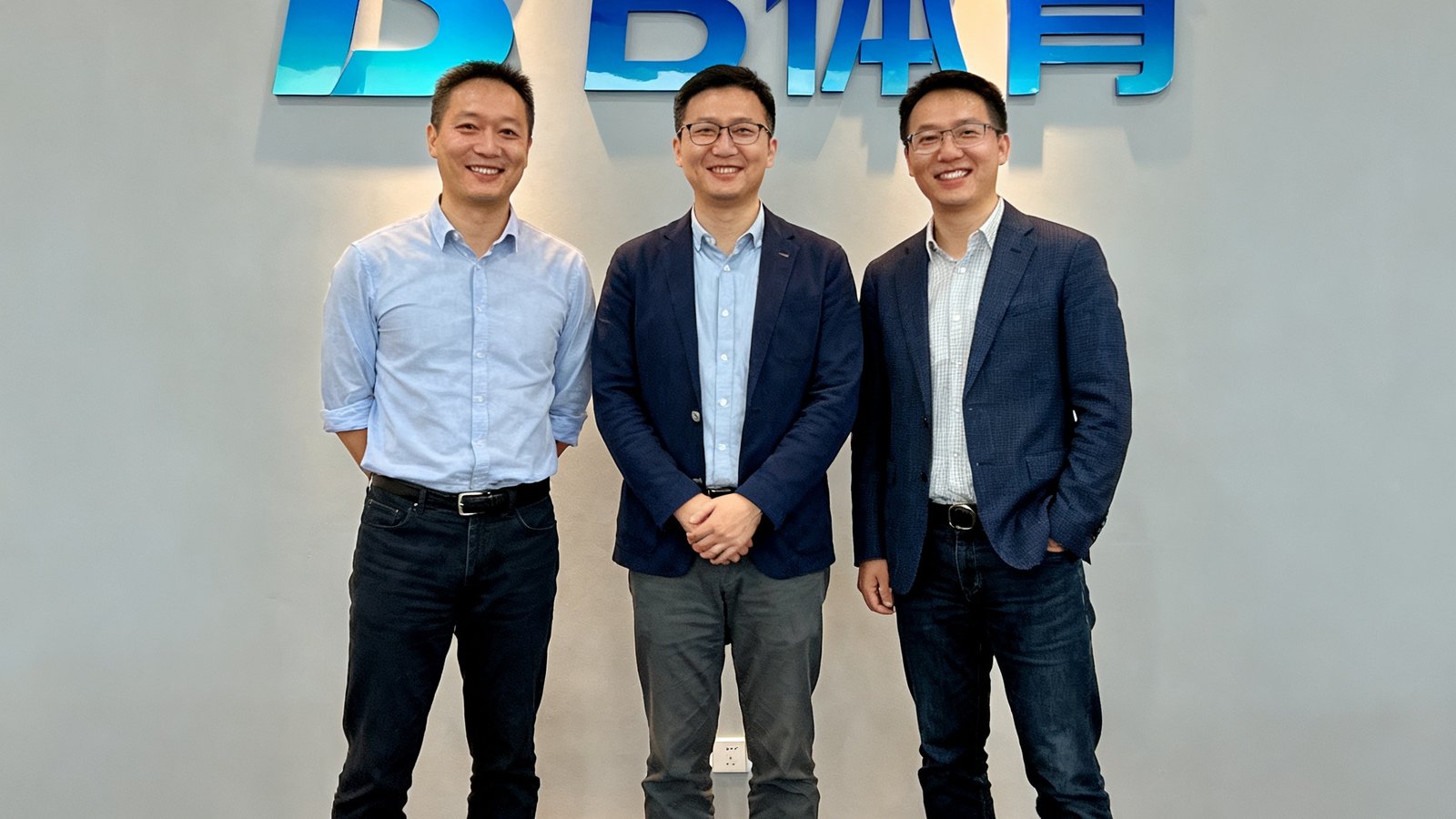 B体育三位联合创始人在公司成立五周年庆典上的合影，三人面带微笑站在印有B体育Logo的背景墙前，穿着休闲商务装，展现出科技创业团队的活力与自信。
